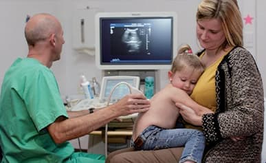 Échographie d'un jeune enfant installé sur les genoux de sa mère (photo d'illustration)